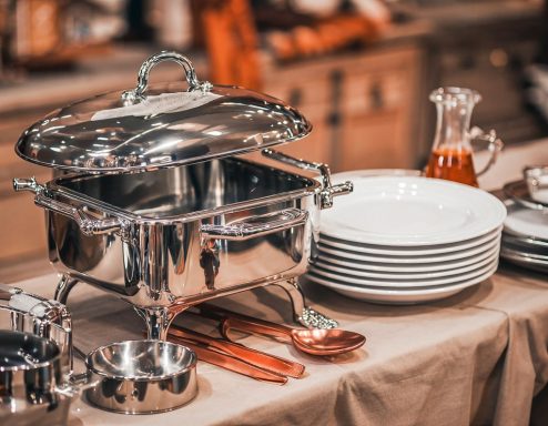 Gastronomieausstattung Elegantes Buffet mit silbernem Speisegeschirr und weißen Tellern auf einem Tisch.