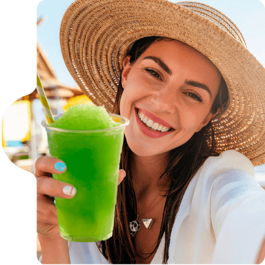 Slush Eine lächelnde Frau mit Sonnenhut hält ein grünes Eisgetränk in der Hand.